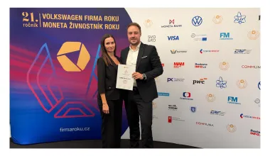 Zwei Personen mit der LOMAX-Urkunde vor der Veranstaltungswand Firma roku 2026