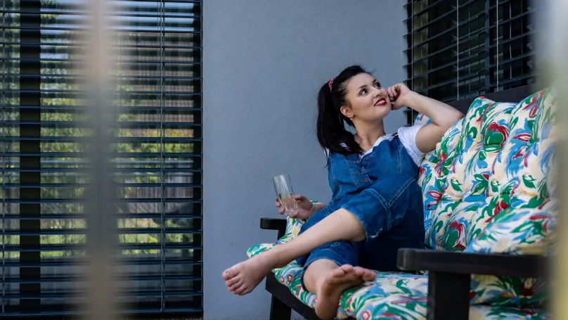 Fenster mit Außenjalousien_Frau auf dem Sofa auf der Terrasse